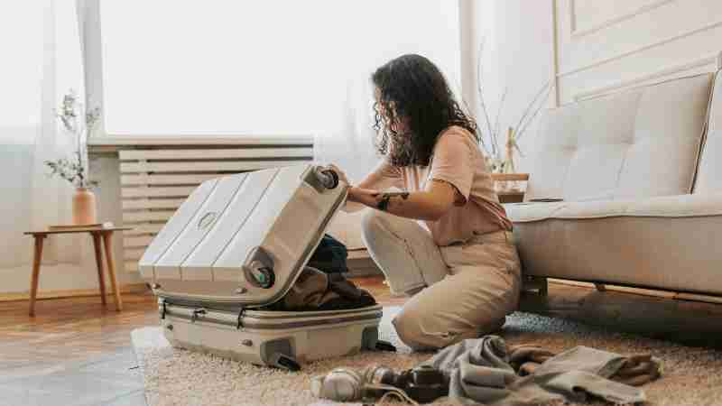 A woman packing her suitcase in a stylish living room, surrounded by clothes and travel accessories., tags: ihr - pexel