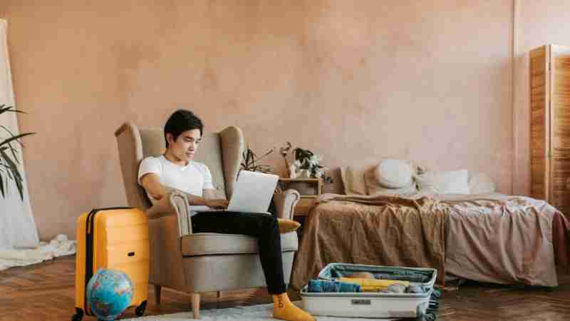 A man uses a laptop while packing a suitcase at home, ready for travel., tags: clevere reisestrategien für - pexel